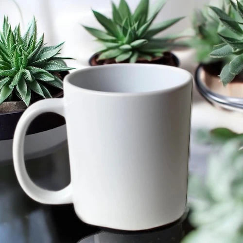 White mug on a reflective surface with green plants in the background