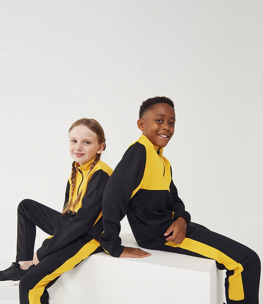 Two children wearing black and yellow tracksuits sitting on a white surface.