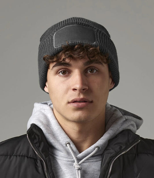 Person wearing a gray beanie and black jacket with a gray background