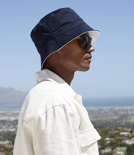 Person wearing a navy bucket hat and sunglasses with a scenic background